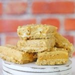 A few squares of no bake peanut butter fudge with cream cheese and a graham crust, stacked up on a wooden dessert plate